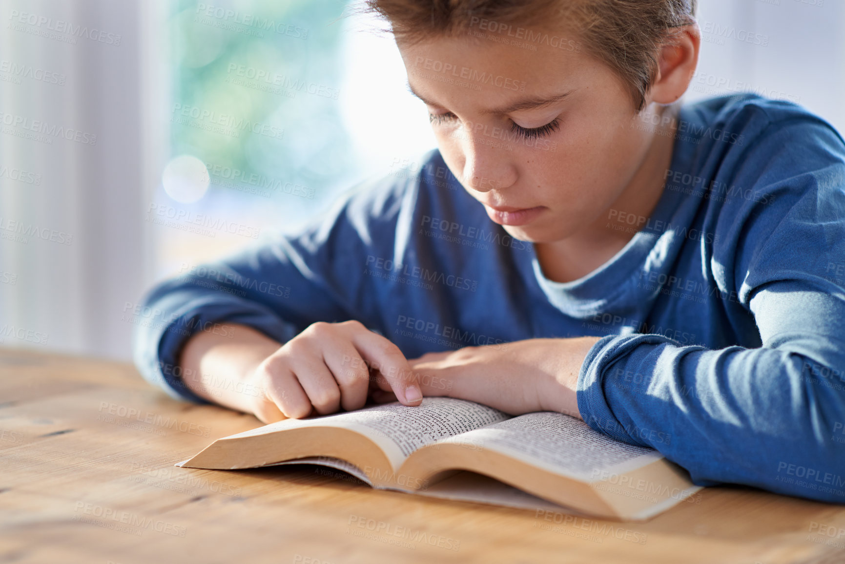 Buy stock photo Shot of a young boy reading a book at a table