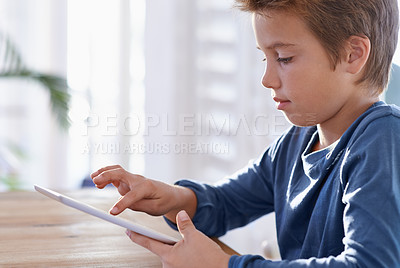 Buy stock photo Shot of a young boy using a digital tablet to do his homework