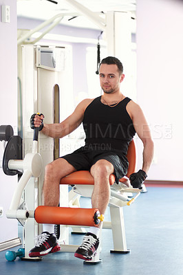 Buy stock photo Portrait of a young man using a gym machine to exercise his leg muscles