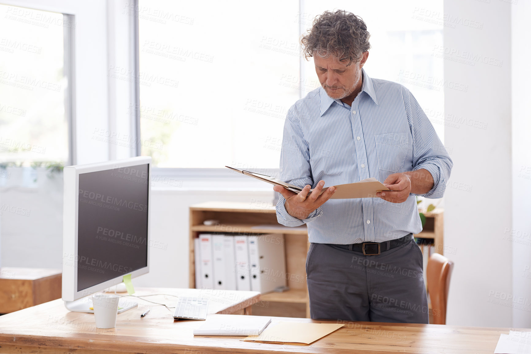 Buy stock photo A businessman looking through a file while standing in his office