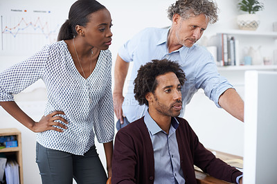 Buy stock photo A team of coworkers standing around a computer and discussing a design