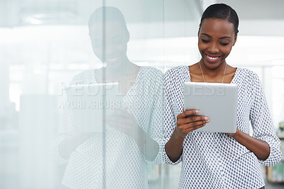 Buy stock photo Shot of a young woman leaning against a glass divider while using a digital tablet