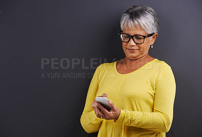 Buy stock photo Glasses, phone and senior woman in studio reading text message, email or blog on internet. Spectacles, technology and elderly female person learning to network on cellphone by black background.