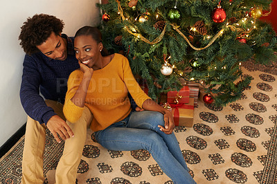 Buy stock photo Shot of an affectionate young couple sitting beside a Christmas tree