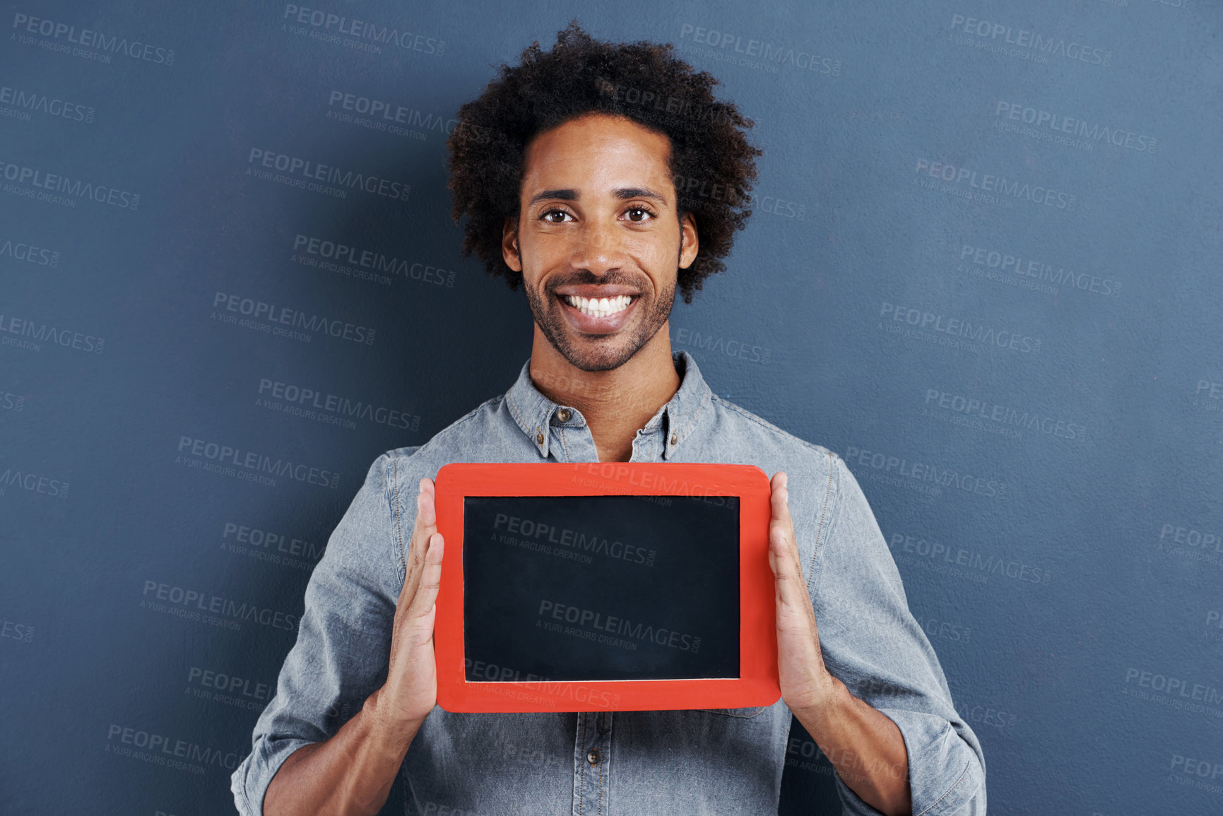 Buy stock photo Portrait of a happy young man holding up a small chalk board on a gray background