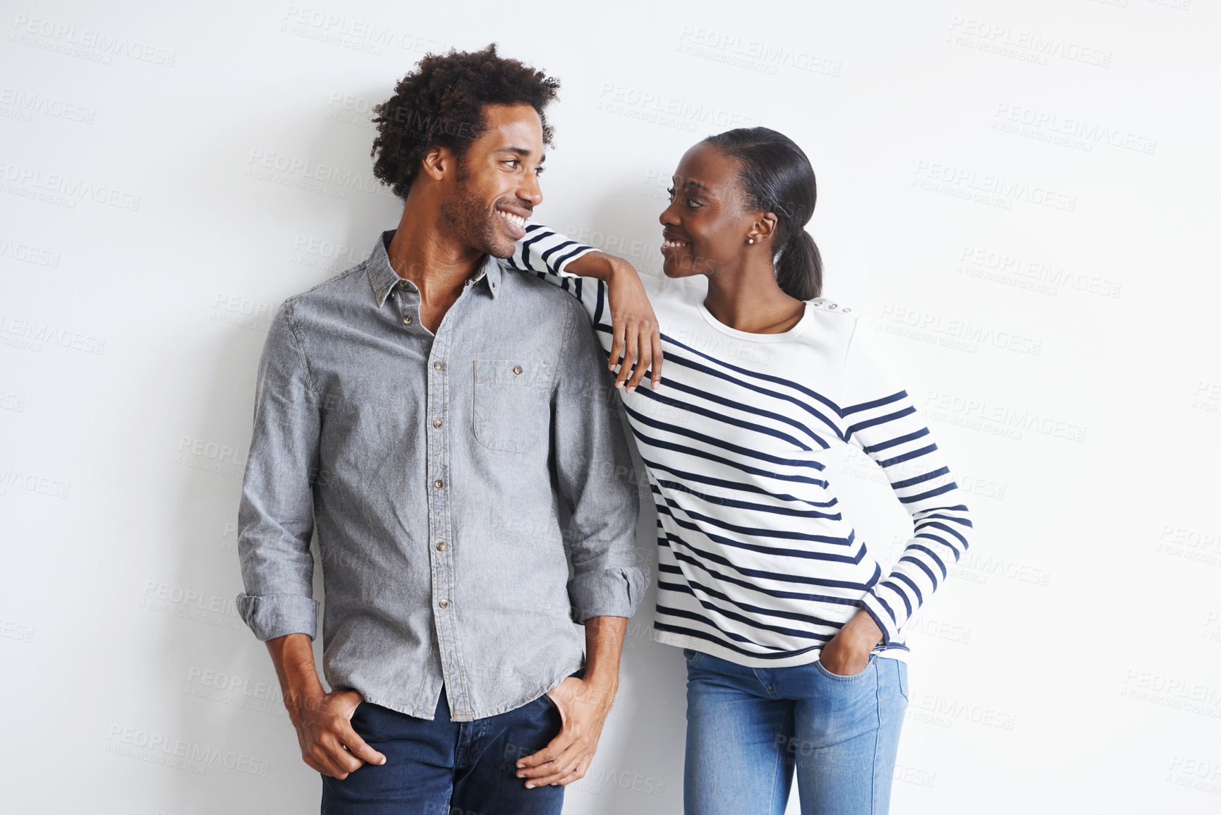 Buy stock photo A happy young couple standing together affectionately against a white wall