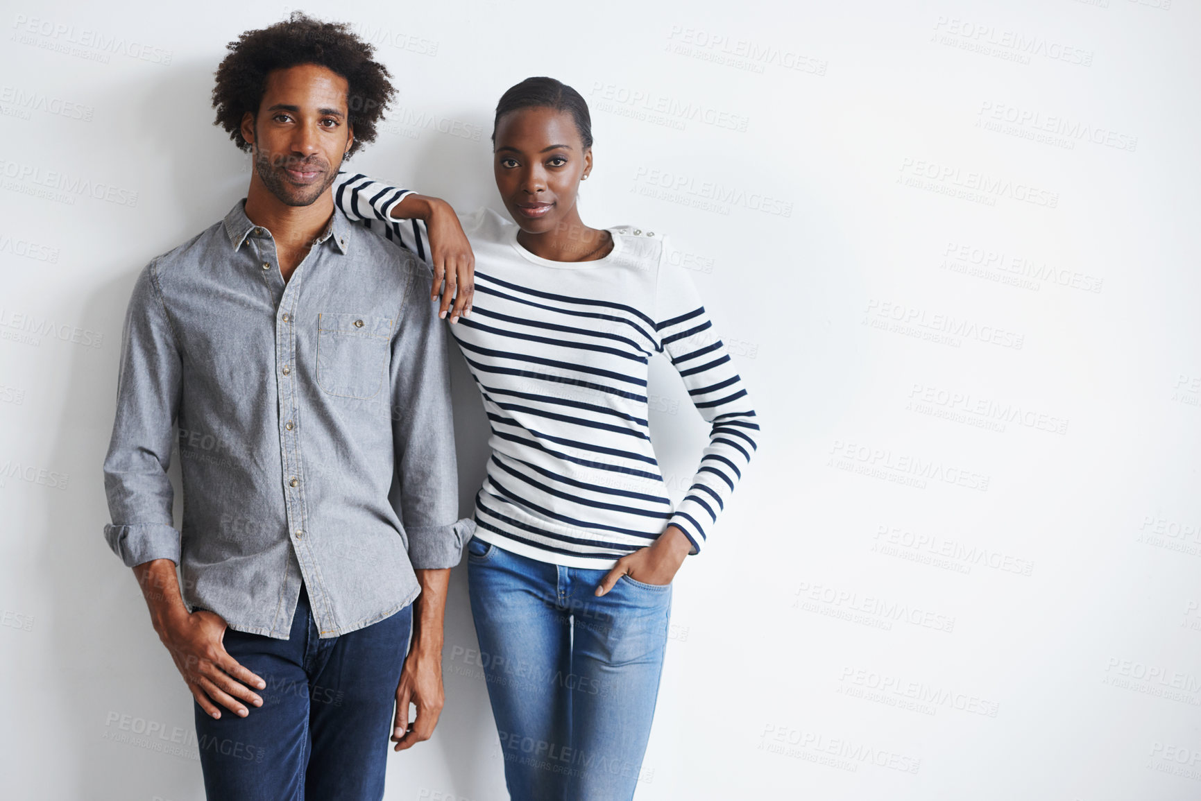 Buy stock photo A portrait of a stylish young couple standing together affectionately against a white wall