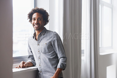 Buy stock photo A portrait of a happy young  man standing and leaning against a window sill