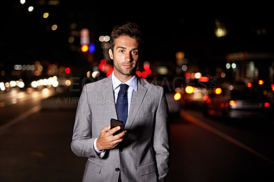 Buy stock photo A portrait of a handsome businessman holding a cellphone while standing in  a busy city street at night