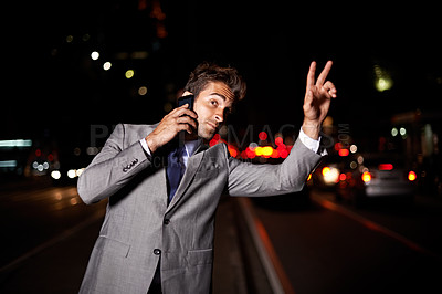 Buy stock photo A handsome businessman hailing a cab while talking on his cellphone in the city at night
