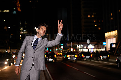 Buy stock photo A handsome businessman hailing a cab while standing in a busy city street at night