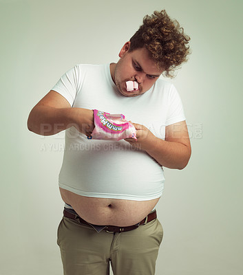 Buy stock photo Obesity, weight gain and comic for man in studio with marshmallow for unhealthy eating, sugar and candy. Overweight person with hand in sweet packet and fat stomach for greed, comedy and humor indoor