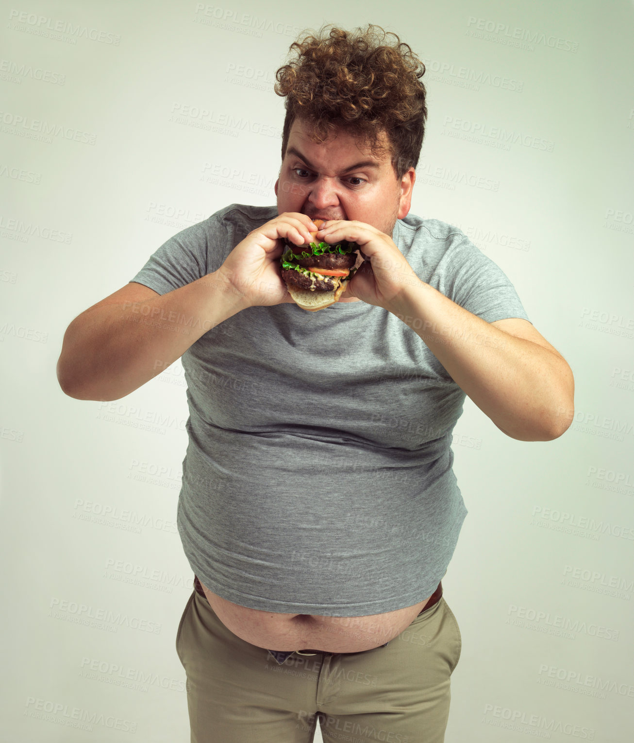 Buy stock photo Obesity, weight gain and burger for man in studio with takeout for unhealthy eating, plus size and greed. Overweight person with meal in mouth and fat stomach for hunger, comedy and bite indoor