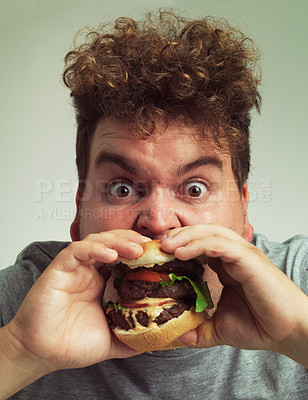 Buy stock photo Takeaway, burger and food for man in studio with meal for big eater, plus size or greed. Young person with meat in mouth for hunger, silly and bite indoor for delicious, taste  and sauce for portrait