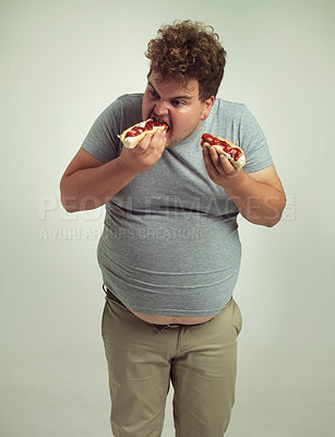 Buy stock photo Plus size man, fast food and eating hotdogs for lunch in studio background for snack, hunger and craving. Male person, hungry and takeaway meal with ketchup or starving and enjoy while standing