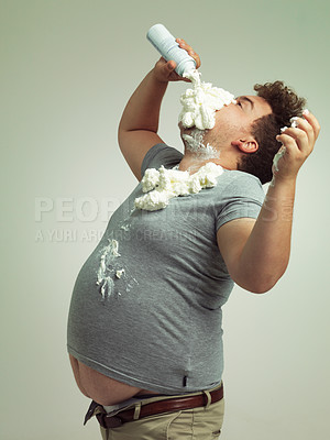 Buy stock photo Plus size, eating and man with cream in studio for unhealthy, sugar and sweet snack or dessert. Messy, greedy and hungry plus size male person enjoying whipped dairy product by gray background.