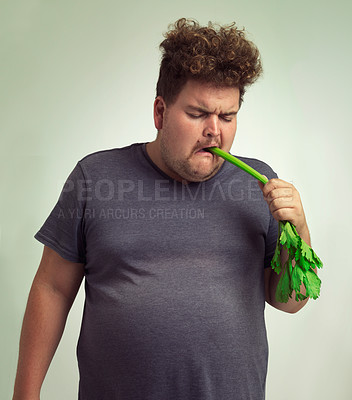 Buy stock photo Diet, plus size and unhappy man eating vegetable for health benefit, nutrition and wellness in studio by white background. Weight loss, celery and male person for healthy food, wellbeing and detox