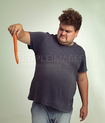 Buy stock photo Plus size, diet and disgusted man with carrot for health, nutrition and wellness in studio by white background. Weight loss, vegetable and unhappy male person for detox, wellbeing and vegan food