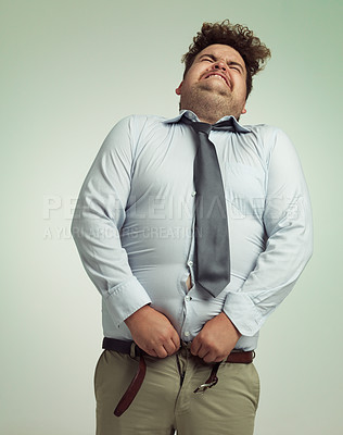 Buy stock photo Humorous studio shot of an overweight businessman trying to button his pants