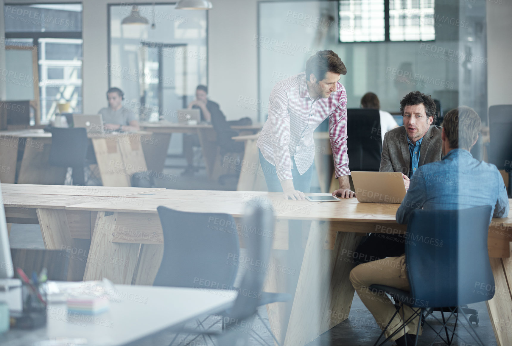 Buy stock photo Through the glass shot of a group of colleagues working together in an office