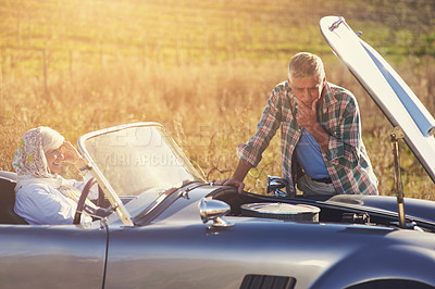 Buy stock photo Shot of a senior man looking under the hood of his car while on a roadtrip with his wife