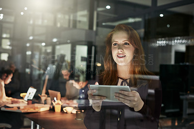 Buy stock photo Shot of an attractive young designer working late at the office with her colleagues in the background