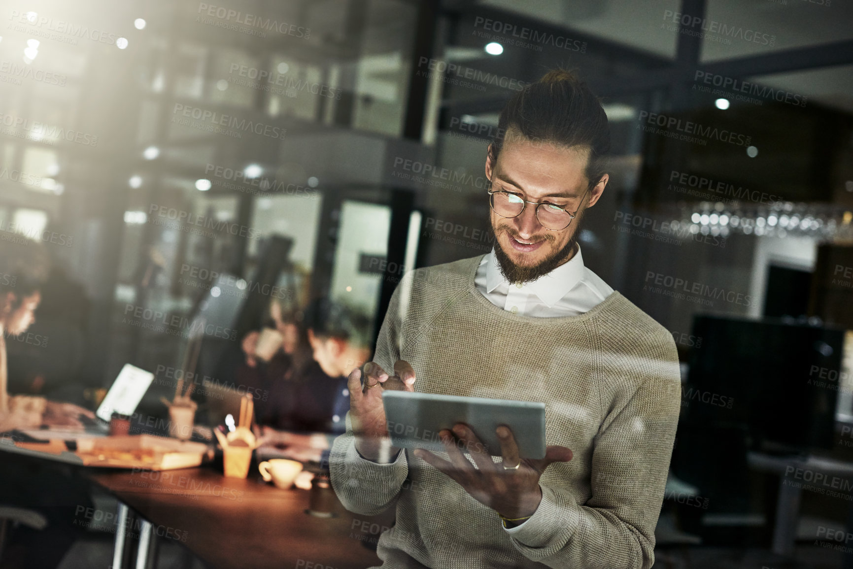 Buy stock photo Shot of a handsome young designer working late at the office with his colleagues in the background