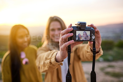 Buy stock photo Shot of two friends taking a selfie with a digital camera while standing outside