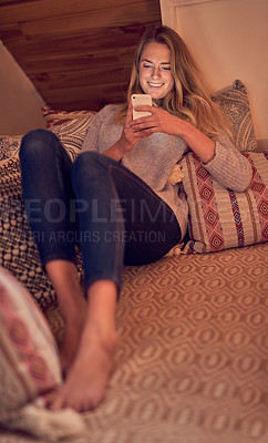 Buy stock photo Shot of a young woman texting on her smartphone while relaxing in her bedroom at home