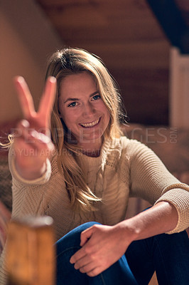 Buy stock photo Portrait of a young woman giving a peace sign while relaxing in her bedroom at home