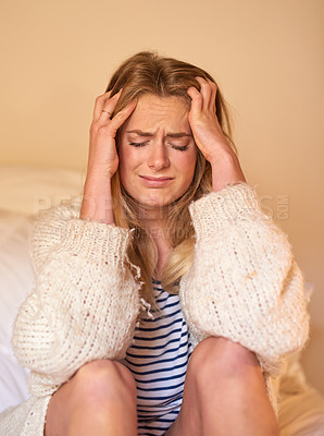 Buy stock photo Shot of a young woman with a headache holding her head while sitting in bed