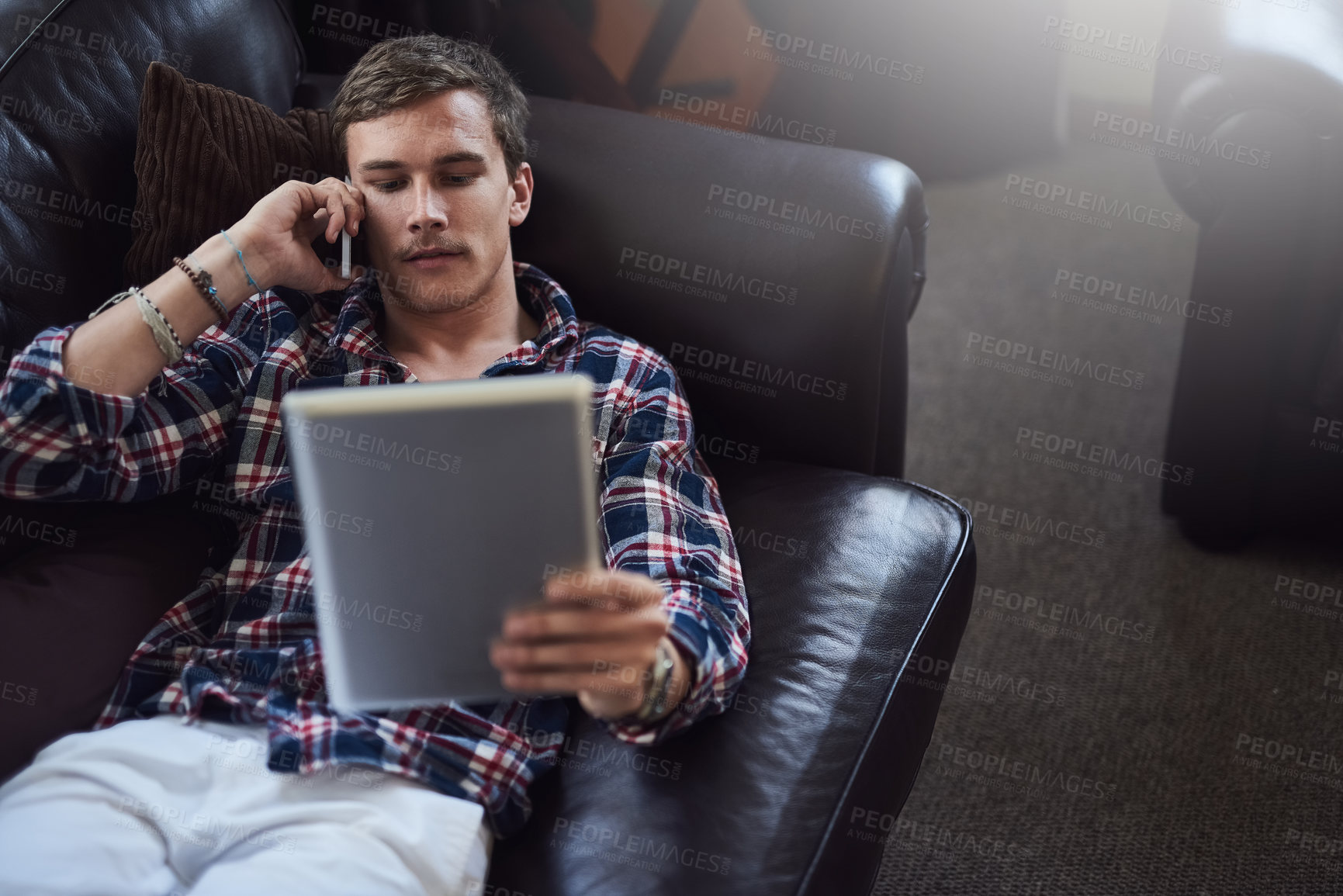 Buy stock photo High angle shot of a handsome young man using his tablet and cellphone while sitting on the sofa at home