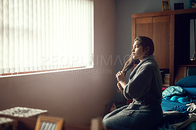 Buy stock photo Shot of a young woman brushing her hair while sitting on her bed in the morning