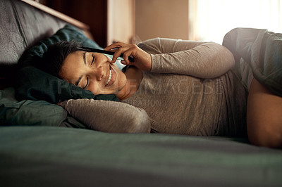 Buy stock photo Shot of a happy young woman answering her phone while lying in bed