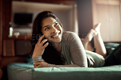 Buy stock photo Shot of a happy young woman chatting on her phone while relaxing in bed