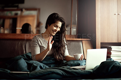 Buy stock photo Shot of a happy young woman video chatting on her laptop while sitting in bed