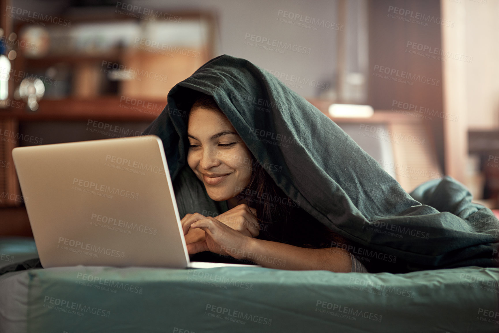 Buy stock photo Shot of a happy young woman using her laptop while lying in bed