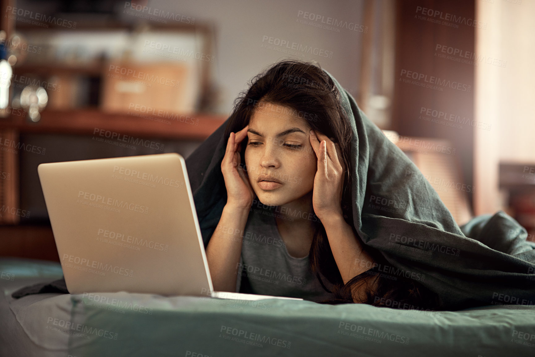 Buy stock photo Shot of a young woman looking at her laptop in dismay as she lies in bed