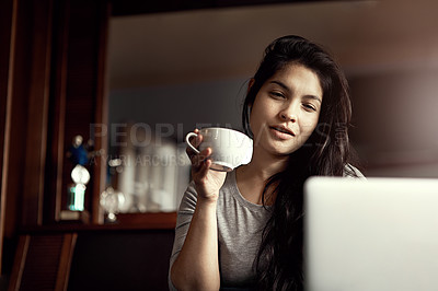 Buy stock photo Shot of a smiling young woman using her laptop while drinking tea in bed