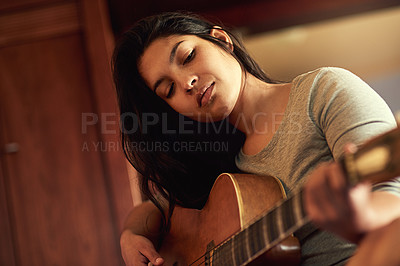 Buy stock photo Shot of a young woman playing her guitar while sitting on her bed