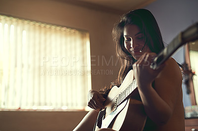 Buy stock photo Shot of a happy young woman playing her guitar while sitting on her bed