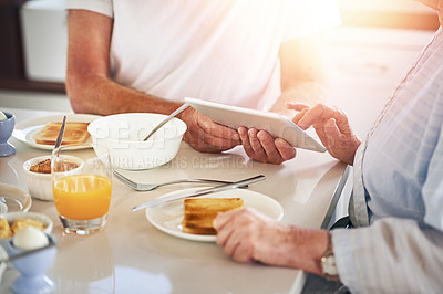 Buy stock photo Closeup shot of a senior couple using a digital tablet while having breakfast at home