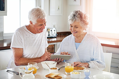 Buy stock photo Cropped shot of a senior couple using a digital tablet while having breakfast at home