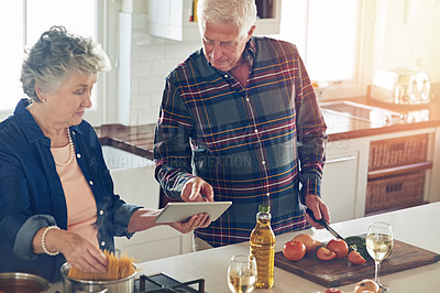 Buy stock photo Cropped shot of a senior couple using a digital tablet while cooking together in their kitchen at home