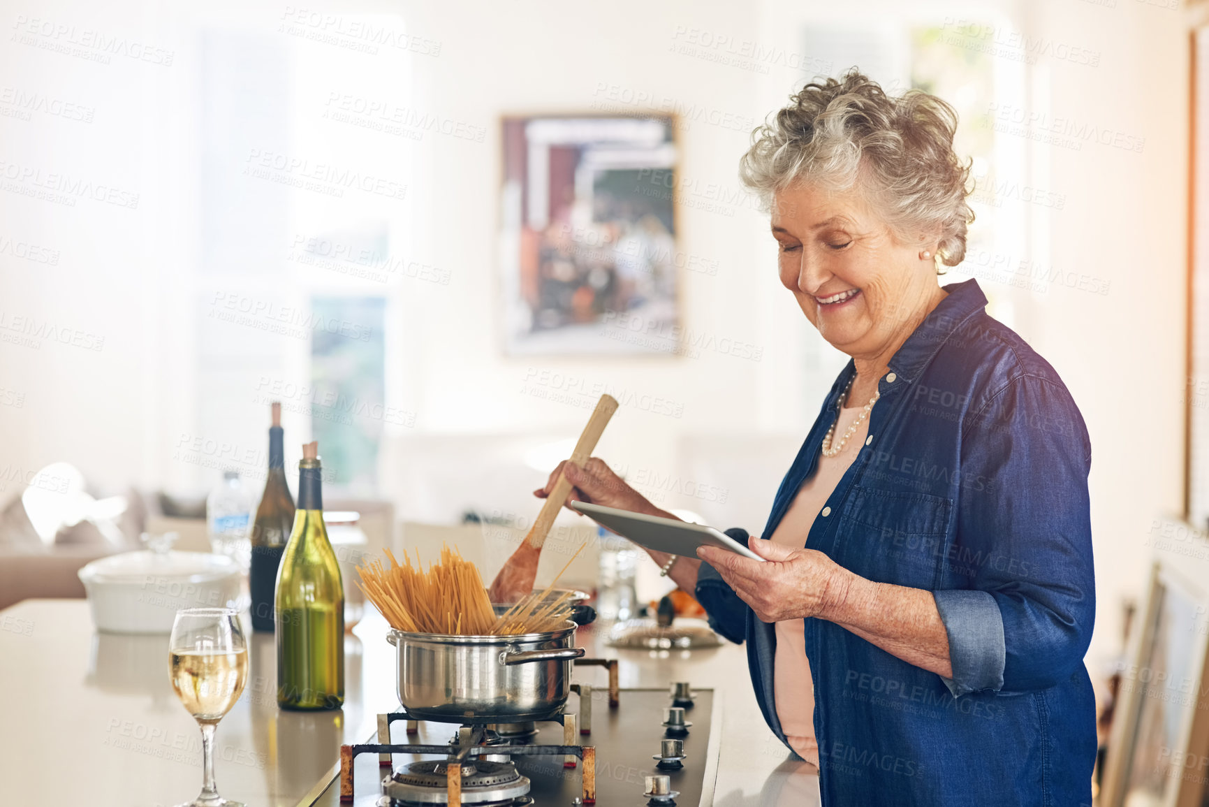Buy stock photo Cropped shot of a senior woman using a digital tablet while cooking in her kitchen