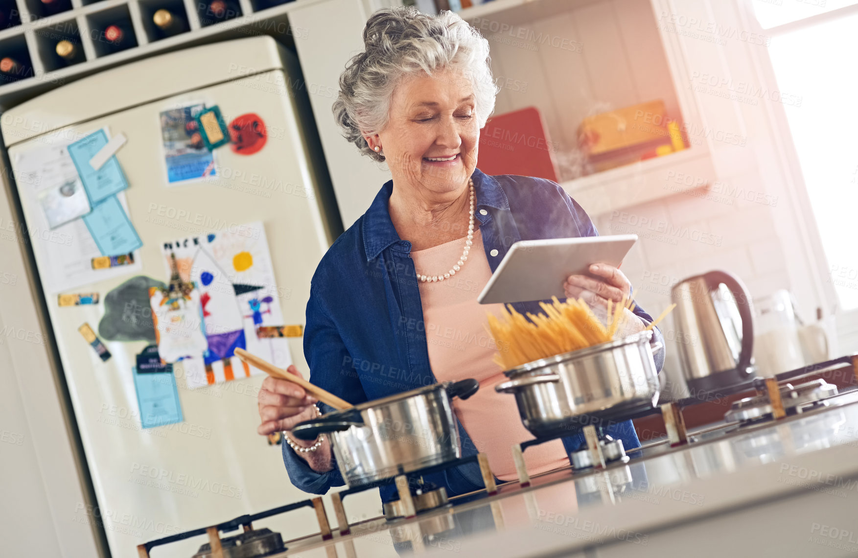 Buy stock photo Cropped shot of a senior woman using a digital tablet while cooking in her kitchen