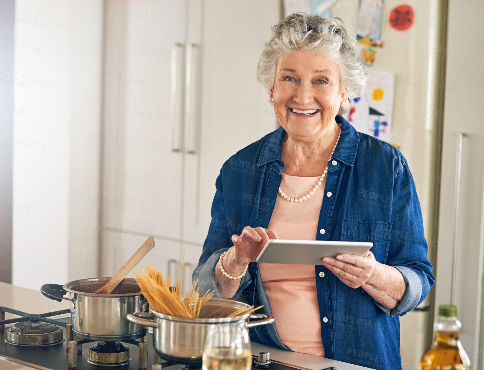 Buy stock photo Portrait of a senior woman using a digital tablet while cooking in her kitchen