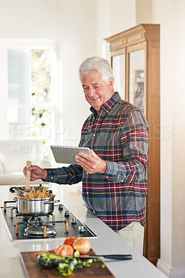 Buy stock photo Cropped shot of a senior man using a digital tablet while cooking in his kitchen