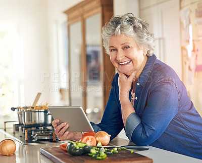 Buy stock photo Portrait of a senior woman using a digital tablet while cooking in her kitchen