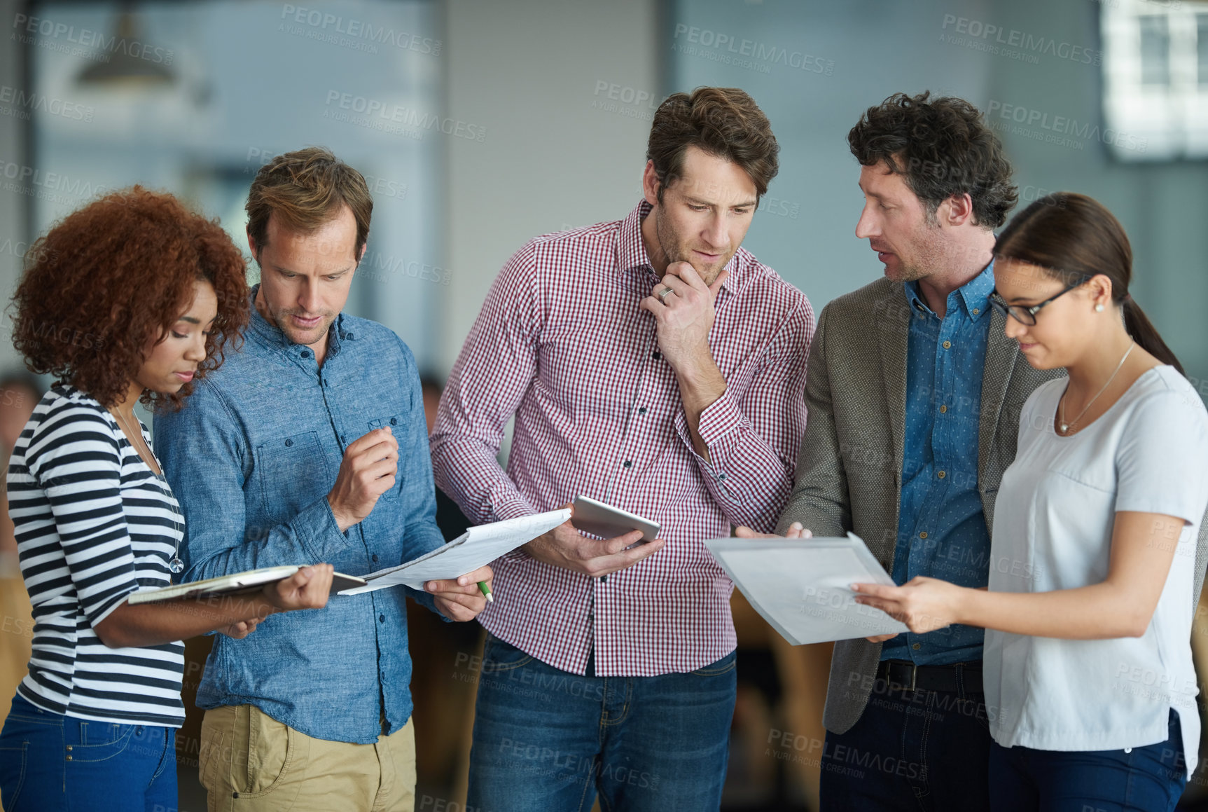 Buy stock photo Colleagues talking about paperwork while standing in the office together. Business people working together to discuss strategy while using wireless devices. Tech savvy ways to save time in your job.